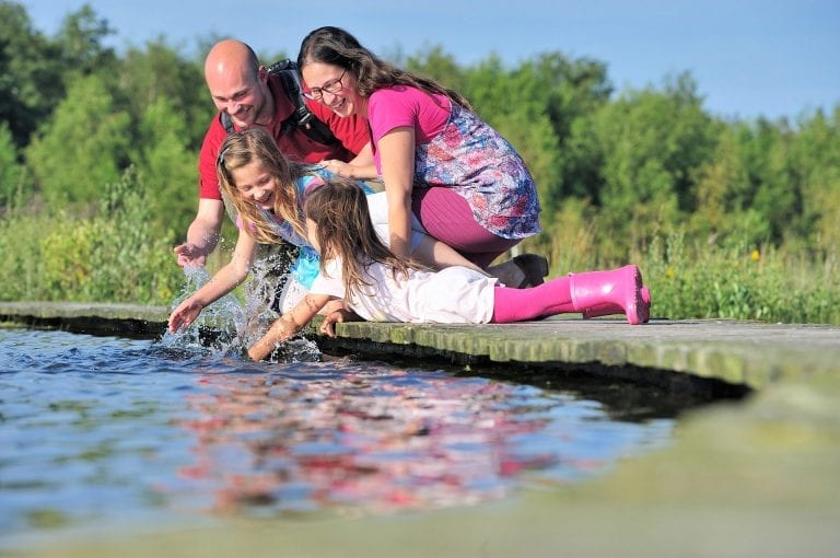 Family in Natuurmonumenten nature reserve Huis ter Heide playing with water on wooden walkway over a pond