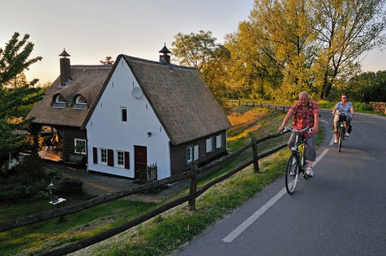 Fietsers op een dijk, met onderaan de dijk een huis