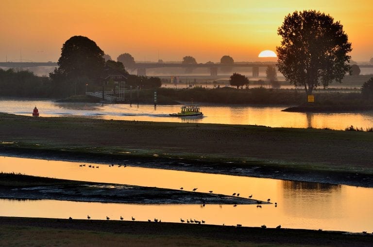 The river Lek at Nieuwegein at sunrise with ship and ferry