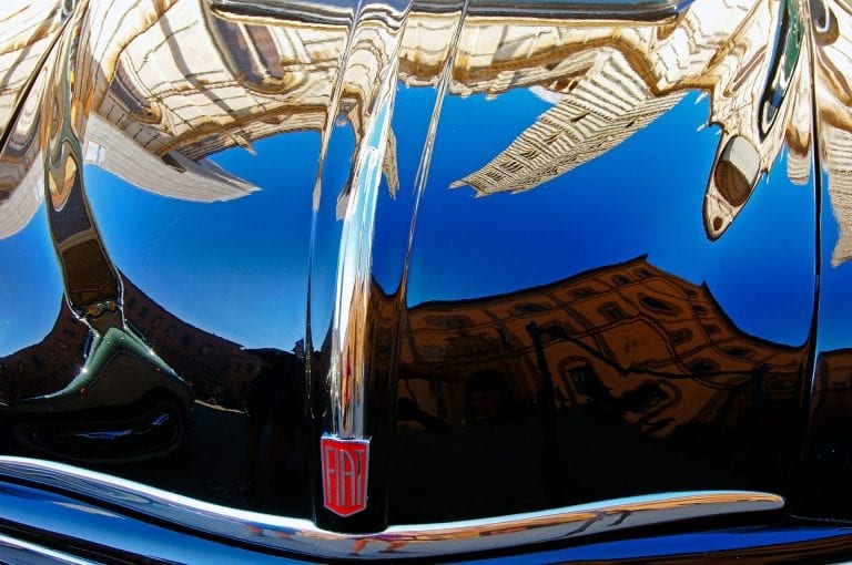 The Siena Cathedral mirrored in the bonnet of a classic Fiat car.