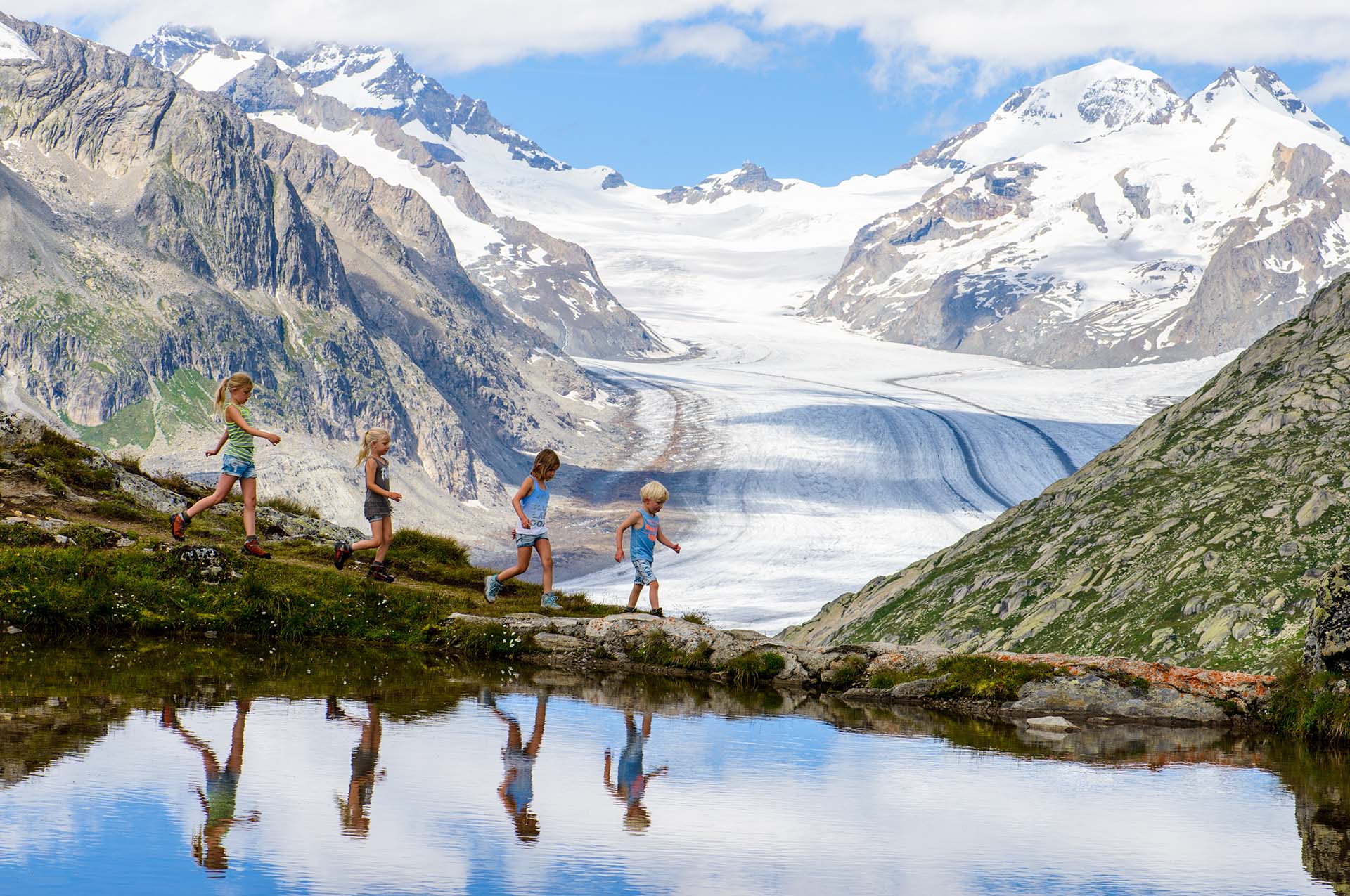 Kids mirrored in water and in background the Aletsch Glacier