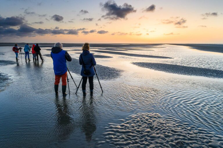 Fotografen op een strand bij zonsondergang, met statieven.