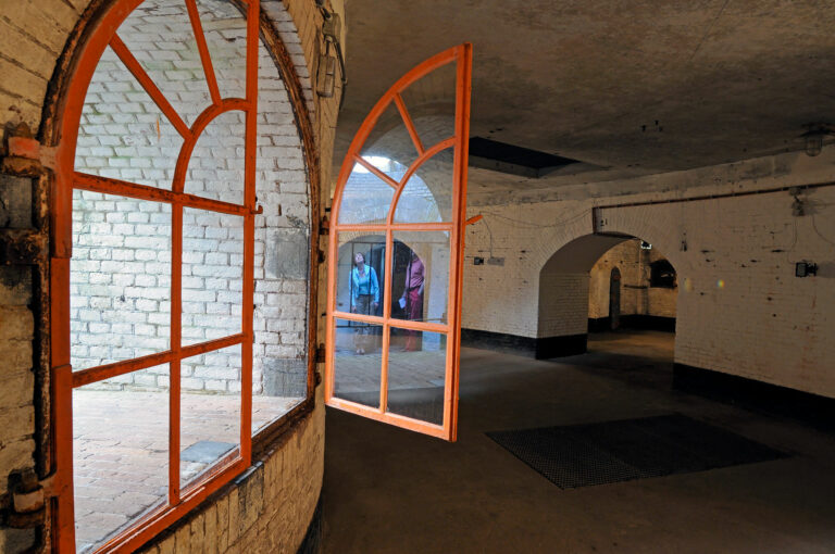 Bezoekers in Fort Asperen, gespiegeld in glas van raam.