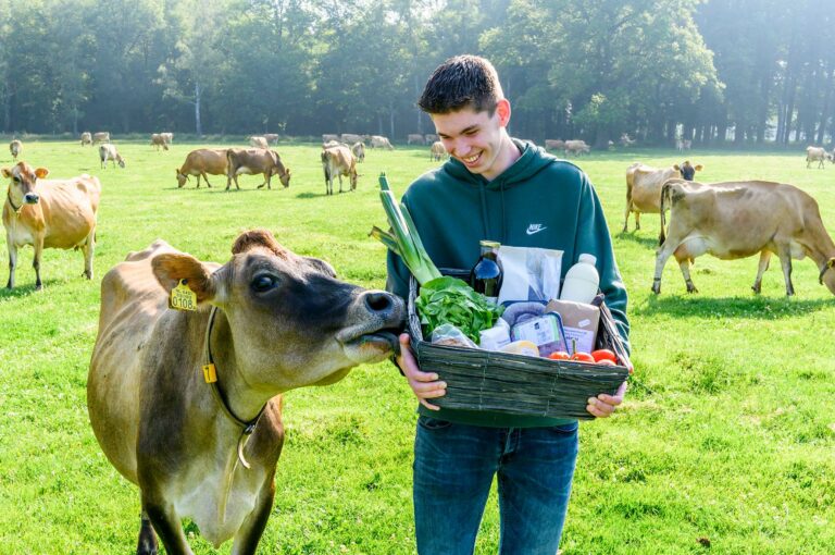 Zoon van de familie Nieuwenburg met koe in weide en mand met biologische producten