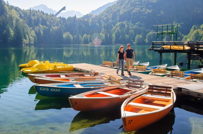 Freibergsee with boats, a couple on the boat pier and a ski jump in the background.