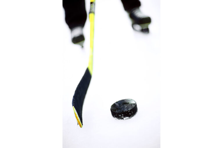 High key image of a man on ice skates holding a stick close to puck