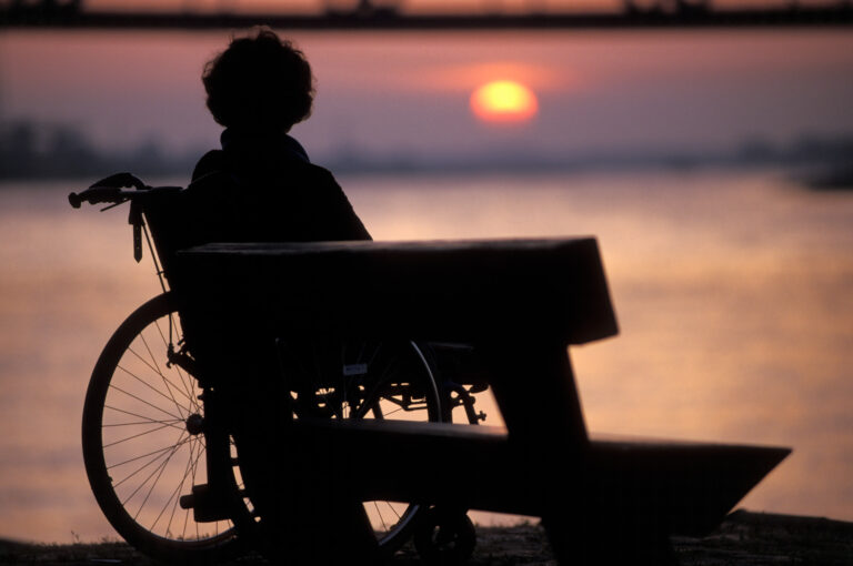 Invalide in rolstoel bij zonsondergang boven Waal bij Nijmegen