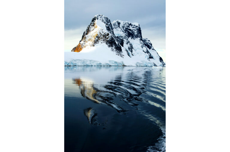 Een besneeuwde kustlijn in de Lemaire Channel, Antarctisch Schiereiland, net aangelicht door het laatste licht van de ondergaande zon.