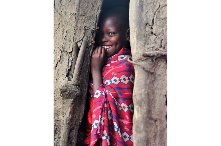 A young Masaï child smiling in the entrance of her hut