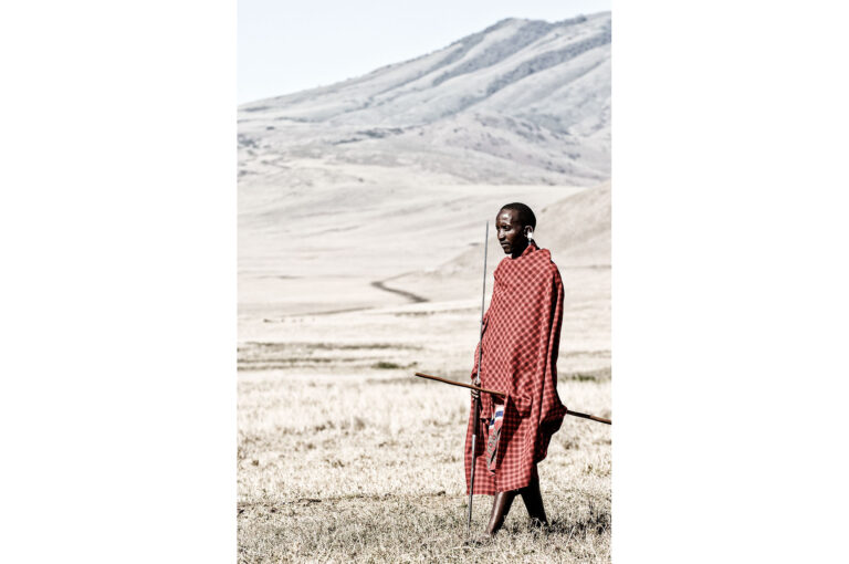 Een Masaï man staat met speer in het landschap