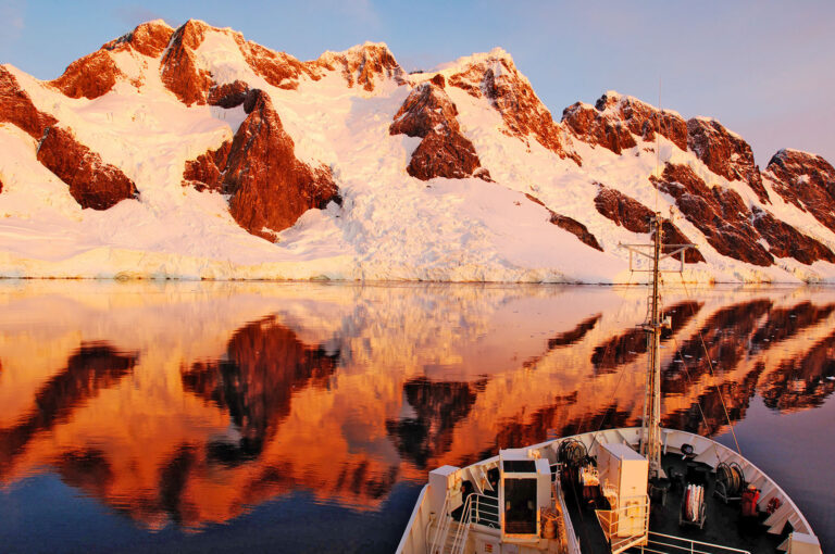 Een expeditieschip ligt voor een door het laatste licht beschenen en besneeuwd eiland in Pleneau Bay Antarctisch Schiereiland, Antarctica.