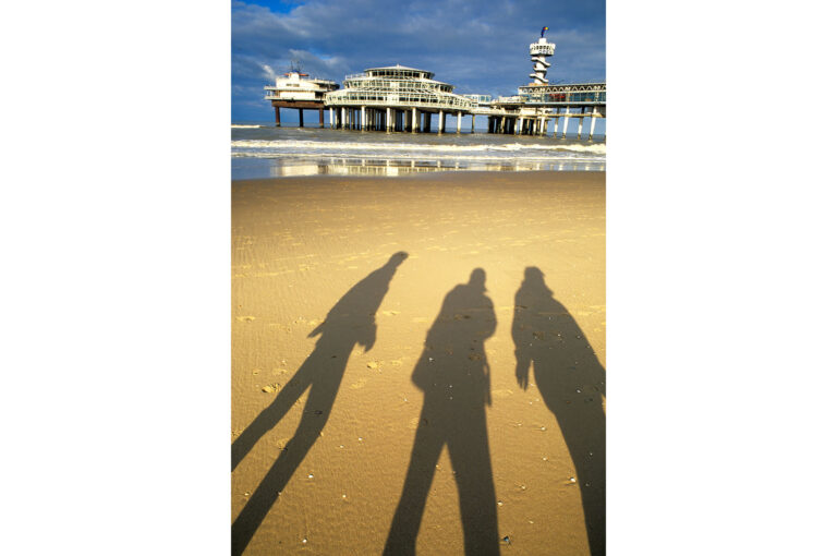 Shadows of people on the beach of Scheveningen, with pier in background.