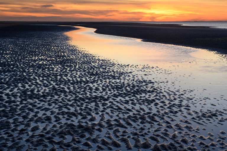 Strand Schiermonnikoog met geul bij eb en zonsondergang.