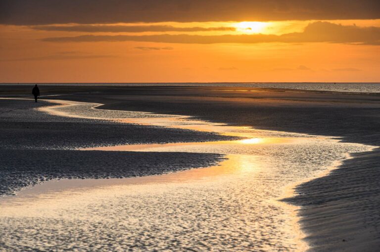 Beach of Schiermonnikoog with beautiful orange sunset, gulley and a human walking