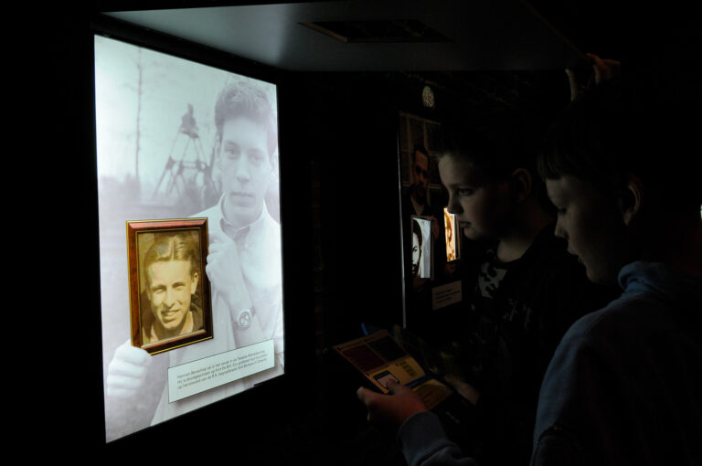 Scholieren kijken naar een paneel waarop een kleinzoon de foto van zijn vermoorde opa laat zien