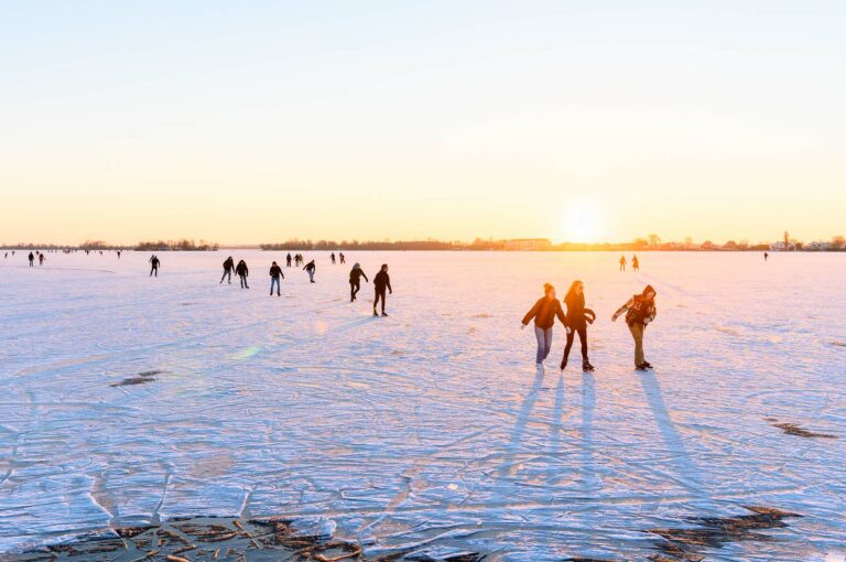 Skaters on frozen lake at sunset