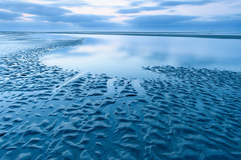 Strand met patronen in water en zand na zonsondergang