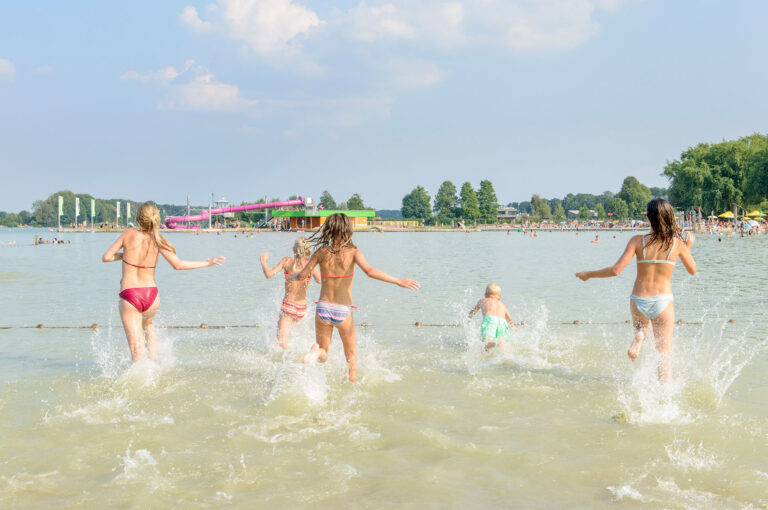Kinderen rennen het water in om te gaan zwemmen.