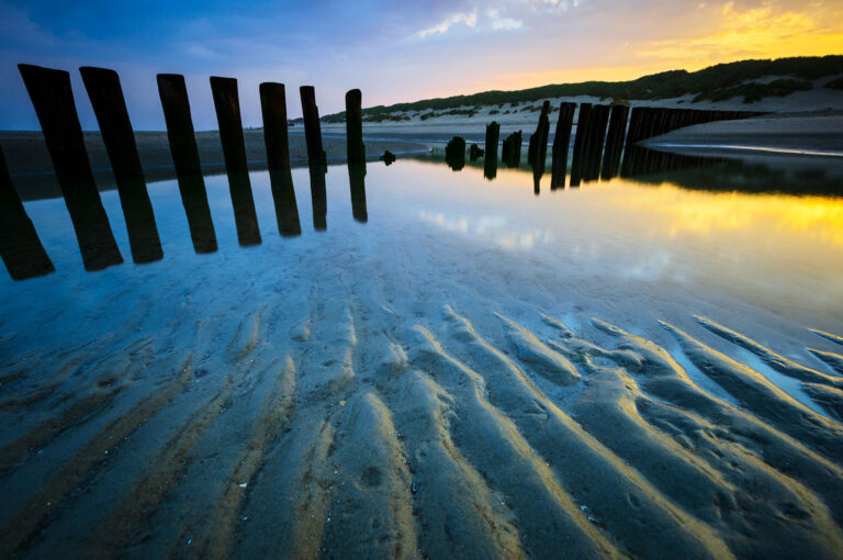 Ribbels op strand en patroon strandpalen bij zonsopkomst