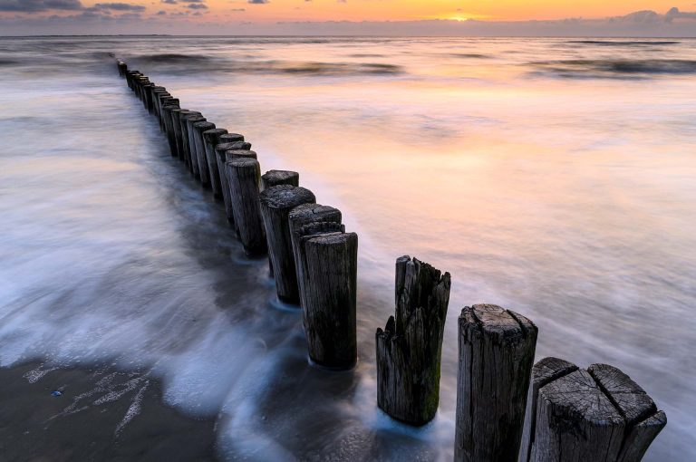 Strandpalen, zee en zonsondergang op Ameland met lange sluitertijd.