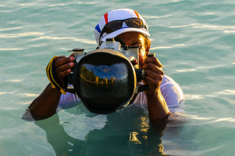 Martin and other photographers mirrored in an underwater camera house, held above water.