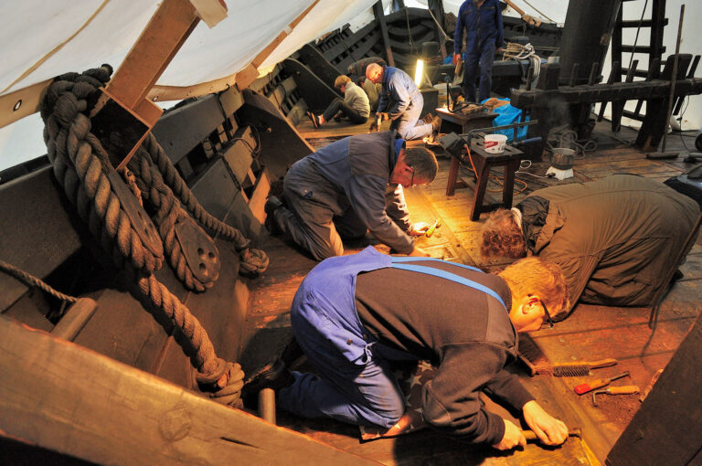 Men and women working on maintenance of an historic ship