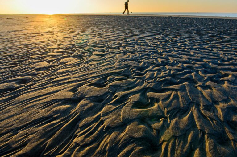 Strand met zandpatronen en wandelaar bij zonsondergang