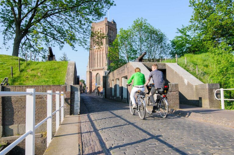 Fietsers rijden Woudrichem binnen door de Koepoort, in achtergrond de Martinuskerk.